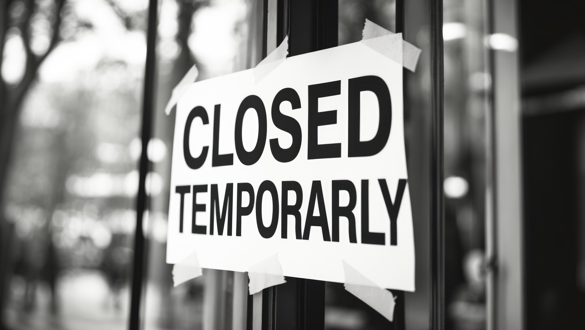 A black and white printed paper sign stating closed, affixed to the glass window or door of a temporarily shut down business storefront.