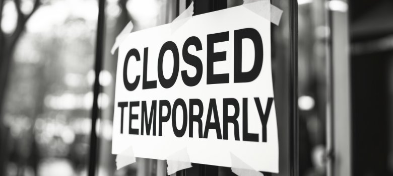 A black and white printed paper sign stating closed, affixed to the glass window or door of a temporarily shut down business storefront.