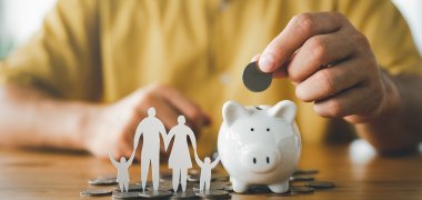 businessman putting coin on the piggybank and paper family on table, donation, saving, charity, family finance plan concept, fundraising, superannuation, investment, financial crisis concept.