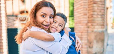Adorable latin student boy and mom hugging at the city.