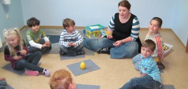 Kinder sitzen im Kreis mit Erzieherin.