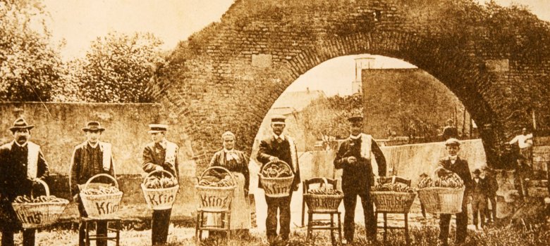 Erinnerungskarte vom ersten Brezelfest 1910 mit Brezelverkäuferinnen und - verkäufern der Speyerer Bäckereien Kling und Keim, versammelt vor dem „Riegel“, der alten Stadtmauer am nördlichen Rand der Speyerer Altstadt. 