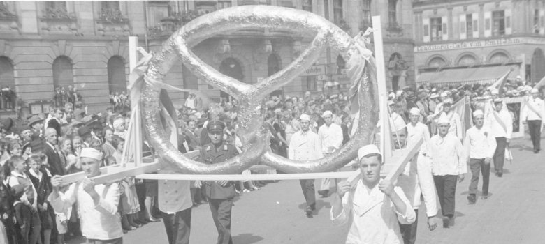 Die Speyerer Bäcker tragen beim Festumzug 1937 eine Riesenbrezel über den Postplatz. 