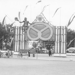 Festvorbereitungen „NACHHER	“: Der Eingang zum Festplatz ist vollendet, geschmückt mit dem Stadtwappen, einer Riesenbrezel und dem „Brezel-Ferdinand“, der auf einen historischen Brezelverkäufer zurückgeht, 1957.