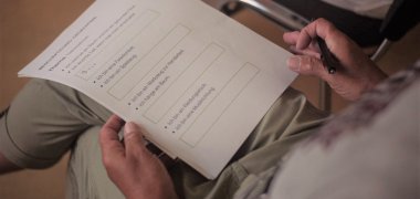 Das Bild zeigte den Schoß einer Person, welche ein Arbeitsblatt in den Händen hält. Auf diesem erkennt man eine Übung zum Gedächtnistraining. Es befasst sich mit der Wortsuche, sogenannten "Teekesselchen".