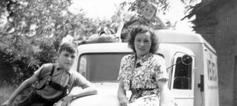 Frau mit Kindern auf Lieferfahrzeug der Nachkriegszeit