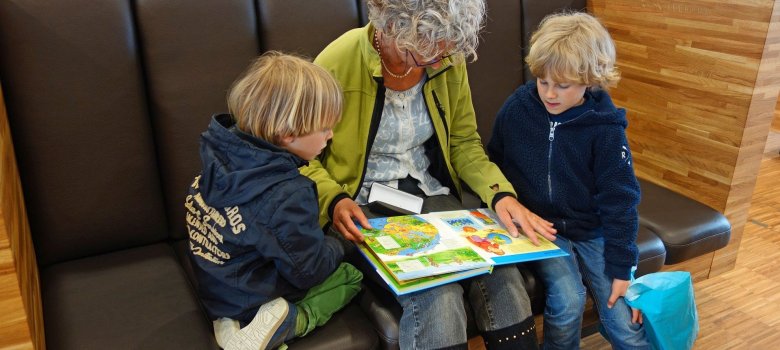Frau liest zwei Kindern aus einem Buch vor