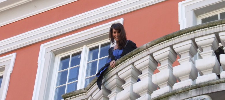 Frau in historischem, mittelalterlichen Gewand steht auf Balkon des Historischen Rathauses Speyer. Ihr Blick geht nach unten.