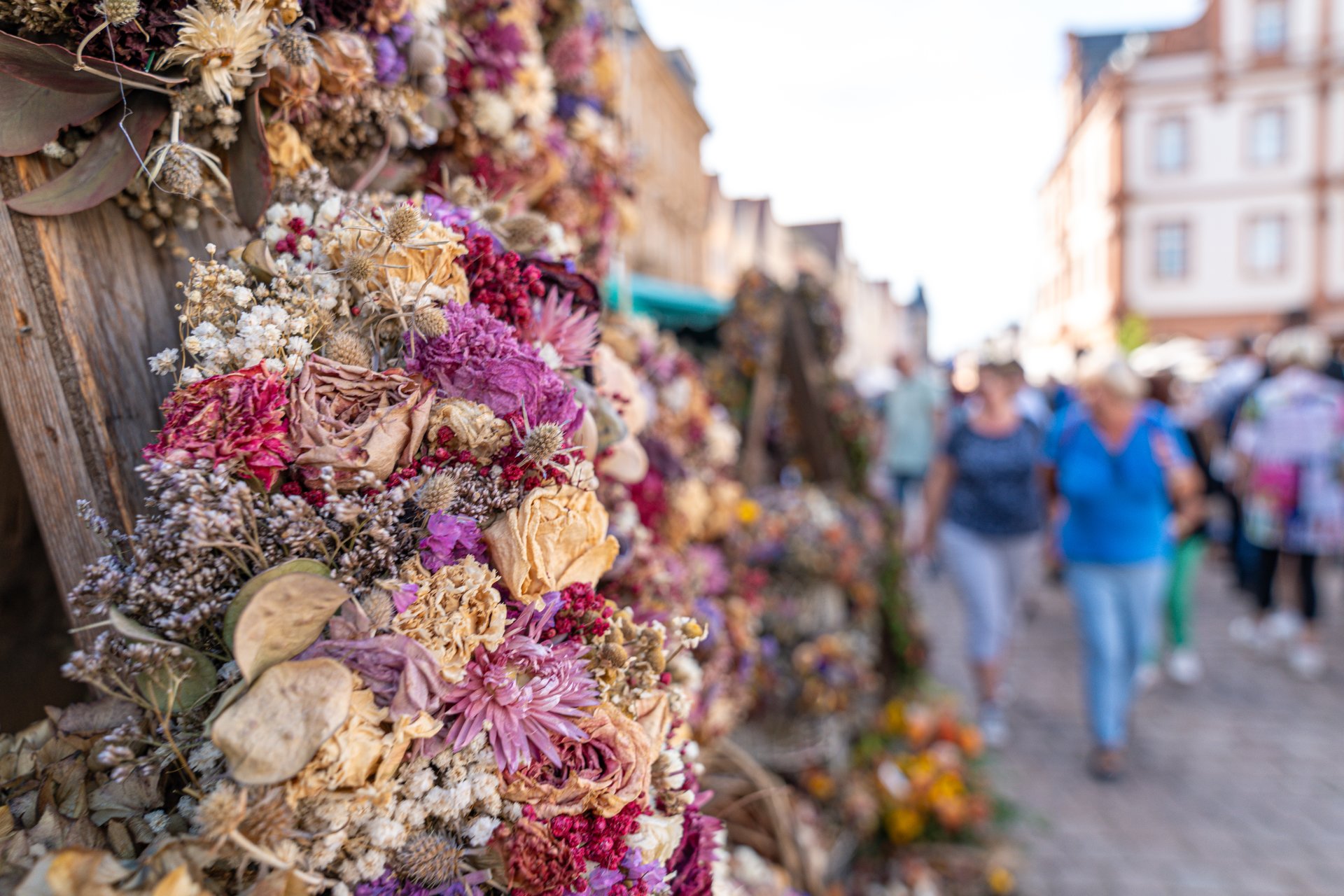 Florale Dekoration an einem verwitterten Holzmast, im Hintergrund geschäftiges Treiben auf der Maximilianstraße in Speyer.