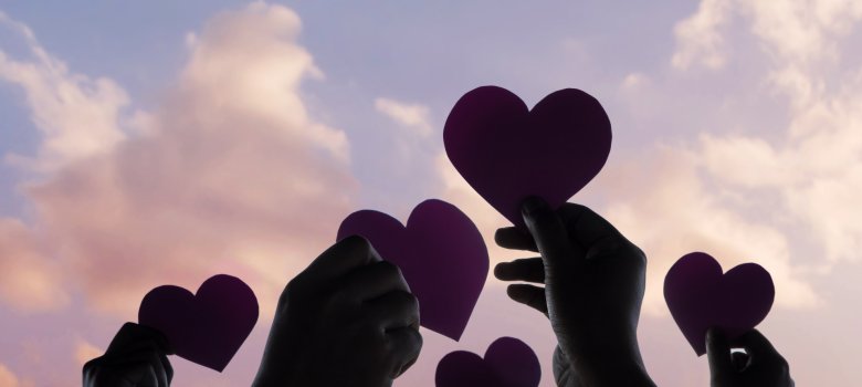 Hände halten ausgeschnittene Papierherzen in den abendlichen Himmel.