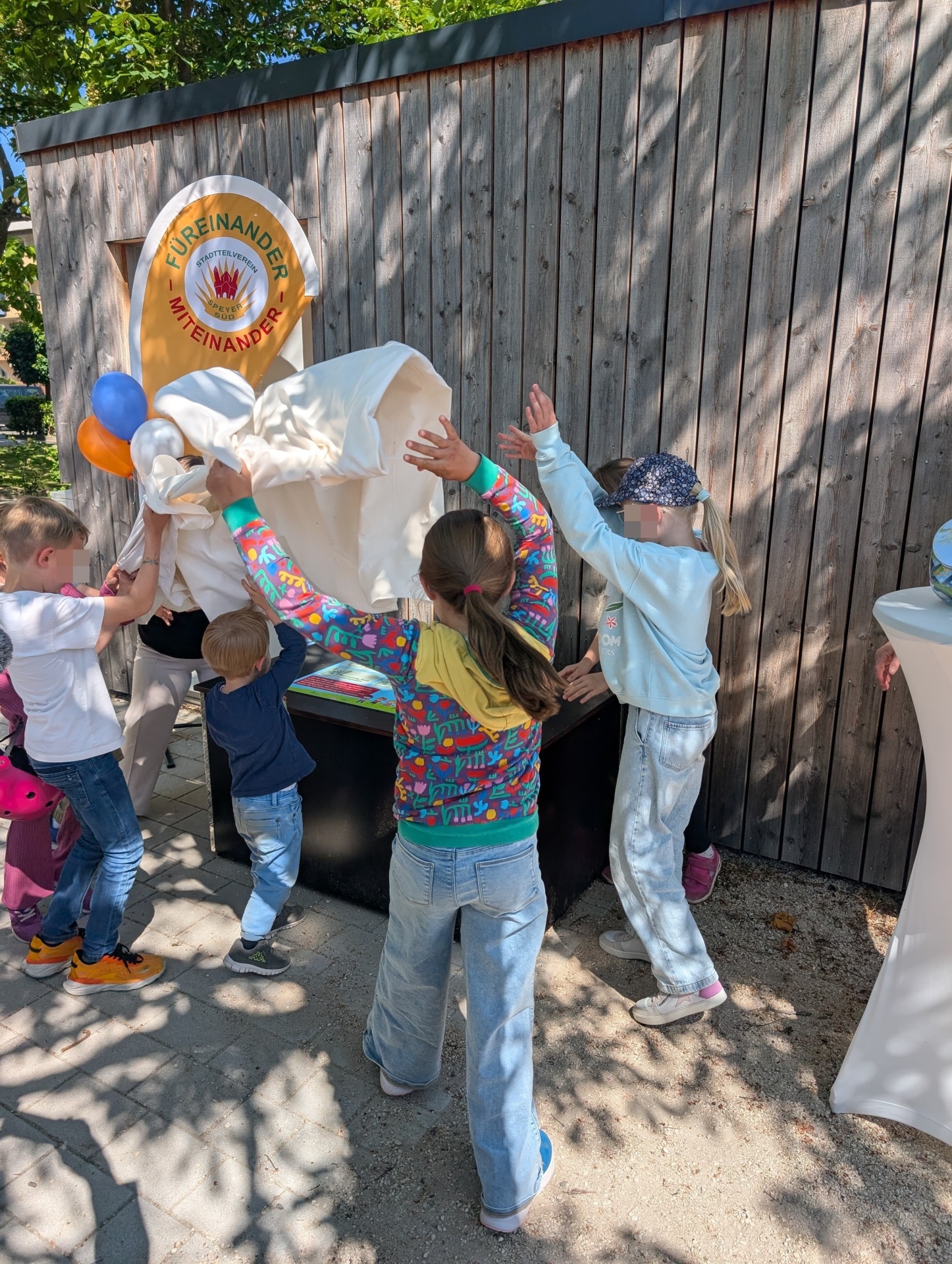 Übergabe der ersten Spielzeug-Ausleihkiste am Platz der Stadt Ravenna im Mai 2025. Viele Kinder stehen um die Kiste herum, ziehen das Tuch weg und enthüllen die Kiste.