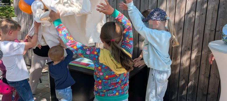 Übergabe der ersten Spielzeug-Ausleihkiste am Platz der Stadt Ravenna im Mai 2025. Viele Kinder stehen um die Kiste herum, ziehen das Tuch weg und enthüllen die Kiste.