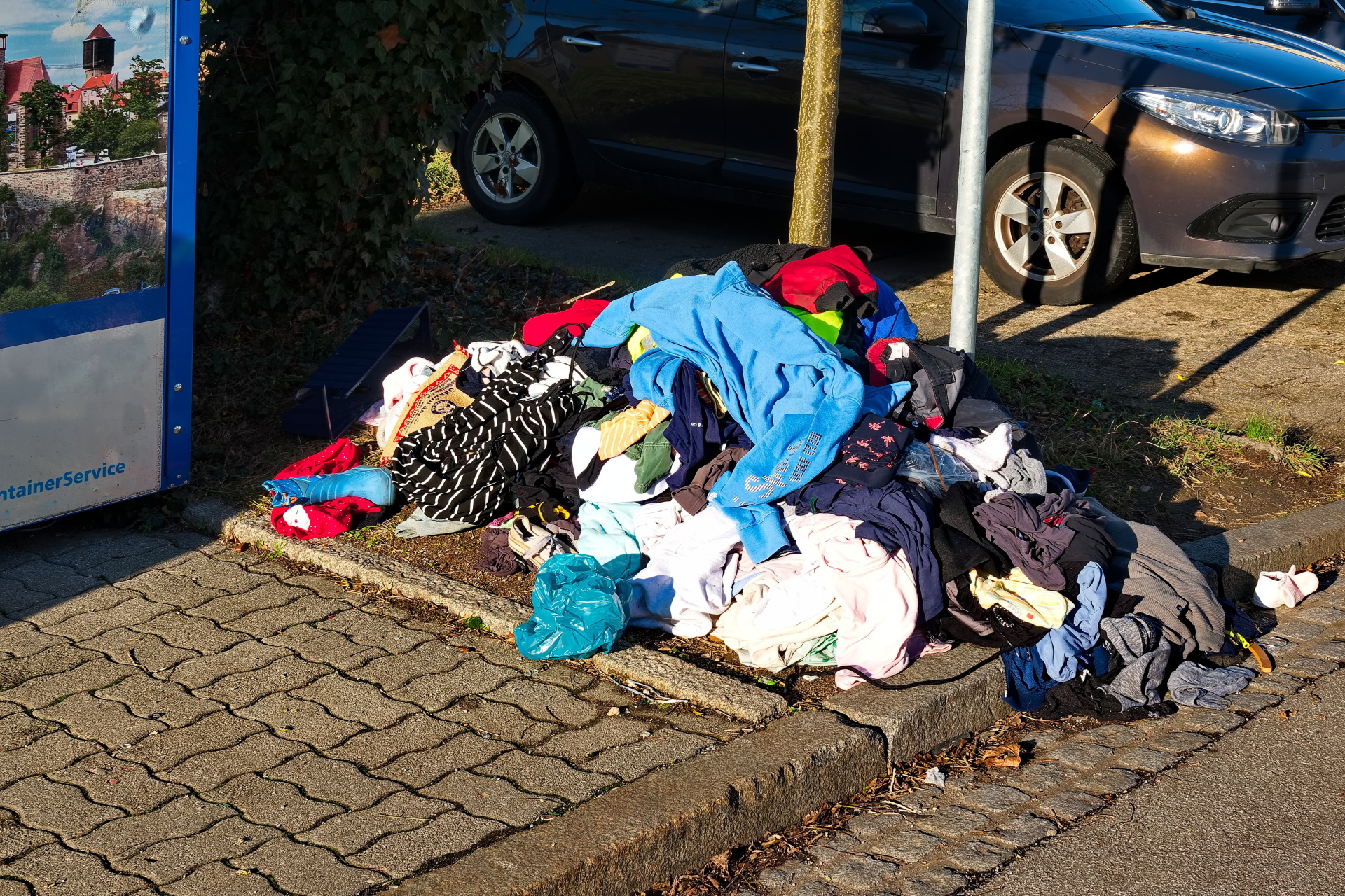 Wahllos Weggeworfene Altkleider neben einen Altkleidercontainer