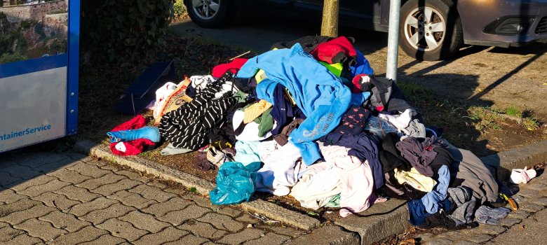 Wahllos Weggeworfene Altkleider neben einen Altkleidercontainer