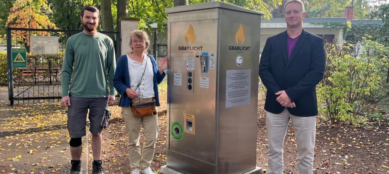Valentin Lind, Beigeordnete Irmgard Münch-Weinmann und Andy Englert (von links nach rechts) präsentieren den neuen Automaten mit den umweltfreundlichen Grablichtern.