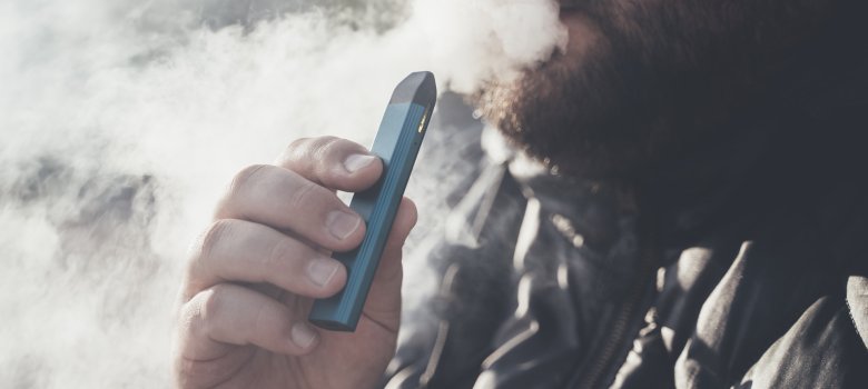 Man smokes new Vape Pod System, inhales and exhales vapor of electronic cigarette, vaping concept