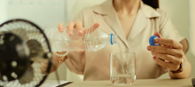 Junge Erwachsene gießt sich Wasser in ihr Glas, vor ihr steht ein kleiner Tischventilator.